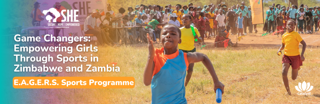 Several young girls are competing in a race across a grassy field under a bright sky. Spectators watch from behind a barrier in the background. The banner in the foreground advertises the S.H.E. Programme's "Game Changers" initiative for girls' sports in Zimbabwe and Zambia.